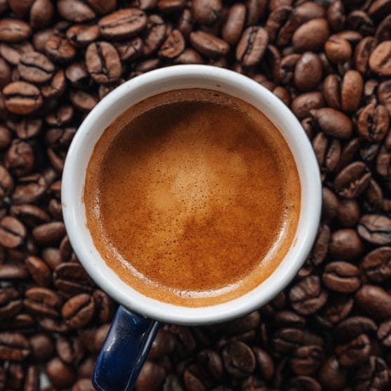 Frischer Espresso mit goldener Crema auf Kaffeebohnen